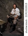 Small photo of Sea robber captain of pirate ship armed with treasure chest in cave. Concept historical halloween. Filibuster cosplay.