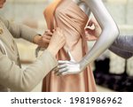 Fashion, dressmaking or tailoring concept. Professional team of tailors, dressmakers or designers working with new model applying linen fabrics beige cloth on mannequin or dummy in atelier