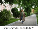 Young adult trendy stylish beautiful caucasian casual woman walking the urban city street with backpack. Female person portrait wear jeans brown trench coat in hurry to meeting. High quality photo