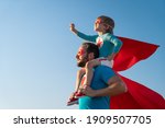 Small photo of Family of superheroes having fun outdoor. Father and son playing against blue summer sky background. Imagination and freedom concept