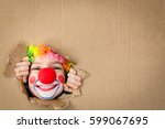 Funny kid clown looking through hole on cardboard. Child playing at home. 1 April Fool's day concept. Copy space.