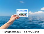 Hand holding a picture of happy big Asian family tourist on vacation with beautiful white clouds on blue sky over calm sea in background.