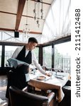 Small photo of A young male waiter in a stylish uniform is engaged in serving the table in a beautiful gourmet restaurant. A high-level restaurant. Table service in the restaurant.