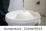 Small photo of A worker using a mixer mixes white putty close-up. Builder mixing white plaster in a bucket using an electric mixer.