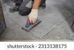 Small photo of Grouting ceramic tiles. Tilers fill the spaces between tiles with a rubber trowel. A professional worker makes repairs. Tiler's hands. House renovation and construction of a new house.