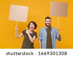 Small photo of Excited protesting two people guy girl pointing index finger on protest signs broadsheet blank placard on stick isolated on yellow background. Protests strikes pickets concept. Youth against city