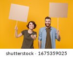Small photo of Funny protesting two people guy girl hold protest signs broadsheet blank placard on stick pointing finger on camera isolated on yellow background. Protests strikes pickets concept. Youth against city