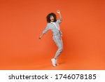 Funny young african american woman girl in gray casual clothes posing isolated on orange background in studio. People lifestyle concept. Mock up copy space. Dancing, standing on toes, rising hands