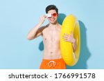 Small photo of Smiling young man guy in eyeglasses isolated on pastel blue wall background. People summer vacation rest lifestyle concept. Mock up copy space. Hold inflatable ring covering eye with credit bank cank