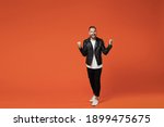 Full length of happy screaming young bearded man wearing basic white t-shirt black leather jacket standing doing winner gesture clenching fists isolated on orange colour background studio portrait