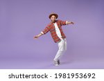 Full length smiling young african american man in casual colorful shirt hat dancing standing on toes spreading hands isolated on violet background studio. People lifestyle concept. Mock up copy space.