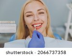 Small photo of Close up young smiling woman choose veneers enamel color palette with stomatologist compare teeth shade sit at dentist office chair indoor light modern cabinet Healthcare enamel whitening treatment.