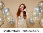 Young stunning redhead woman 20s in evening dress near balloons doing phone gesture like says call me back isolated on plain pastel beige background studio portrait. Celebrating birthday party concept