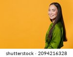 Side view of smiling charming pretty attractive beautiful young brunette asian woman 20s wearing basic green shirt standing looking camera isolated on bright yellow colour background, studio portrait