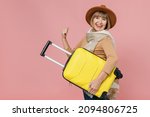 Small photo of Traveler tourist mature elderly senior woman 55 years old wears brown shirt hat scarf hold under hand suitcase bag clench fists say yes isolated on plain pastel light pink background studio portrait