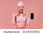 Small photo of Young happy woman with bright dyed rose hair in rosy top shirt hat hold in hand use mobile cell phone with blank screen workspace area do winner gesture isolated on plain light pastel pink background