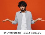 Small photo of Shocked young bearded Indian man 20s years old wears blue shirt spreading hands shrugging shoulder standing questioned and unaware nothing to say isolated on plain orange background studio portrait