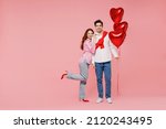 Full body young couple two friends woman man in shirt hold bunch of red inflatable balloons hug isolated on plain pastel pink background studio portrait. Valentine's Day birthday holiday party concept