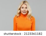 Small photo of Elderly sad shocked disappointed distemepered, unnerved blonde caucasian woman 50s in orange turtleneck look camera isolated on plain grey color background studio portrait. People lifestyle concept