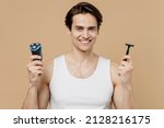 Small photo of Attractive young man he 20s perfect skin in undershirt hold choice electric plastic disposable razor choose isolated on pastel light beige background. Skin care healthcare cosmetic procedures concept