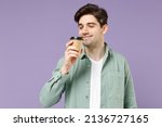 Small photo of Young excited satisfied fun man 20s in casual green mint shirt white t-shirt holding paper cup of coffee drink hot tea in morning sniff with closed eyes isolated on purple background studio portrait