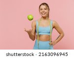 Small photo of Young strong sporty athletic fitness trainer instructor woman wear blue tracksuit spend time in home gym toss up apple hold measure tape isolated on pastel plain pink background. Workout sport concept