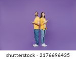 Full body side view young couple two friends family man woman together in yellow clothes hold in hand use mobile cell phone stand back to back browsing internet isolated on plain violet background.