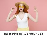 Small photo of Young caucasian redhead woman 20s ginger long hair wearing straw hat glasses summer clothes show blah blah gesture ja jaja hands looking aside isolated on pastel pink color background studio portrait