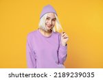 Small photo of Smiling young blonde caucasian woman 20s bob haircut bright makeup wearing basic purple shirt violet beanie hat looking camera playing with hair isolated on yellow color background studio portrait