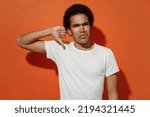 Small photo of Distempered irritated dissatisfied sullen unnerved young black curly man 20s years old wears white t-shirt showing thumb down dislike gesture isolated on plain pastel orange background studio portrait