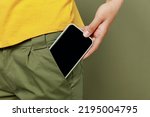 Close up cropped photo shot woman she wear yellow t-shirt holding in hand put into pants pocket mobile cell phone with blank screen workspace area card isolated on plain olive green khaki background.