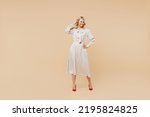 Full size body length blithesome elderly gray-haired blonde woman lady 40s years old wears pink dress hold hand on waist looking down posing isolated on plain pastel beige background studio portrait