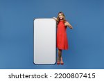 Full body young woman 30s wear red dress big huge blank screen mobile cell phone with workspace copy space mockup area show thumb up isolated on plain dark royal navy blue background studio portrait