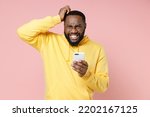 Small photo of Preoccupied young man 20s wearing casual yellow streetwear hoodie using mobile cell phone typing sms message put hand on head isolated on plain light pastel pink color background studio portrait