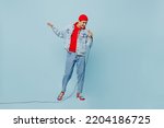 Full body young singer middle eastern man 20s he wear denim jacket red hat sing song in microphone at karaoke club isolated on plain pastel light blue cyan background studio. People lifestyle concept