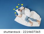 Full length top view young latecomer man in pajamas jam sleep mask rest at home lie wrap covered under blanket hold face slept late isolated on dark blue sky background Bad mood night bedtime concept