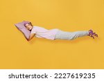 Small photo of Full body side view young woman she wears purple pyjamas jam sleep eye mask rest relax at home fly fall hover over head on pillow isolated on plain yellow background studio portrait. Night nap concept