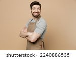 Small photo of Young man barista barman employee wear brown apron work in coffee shop hold hands crossed folded look aside on workspace isolated on plain pastel light beige background. Small business startup concept