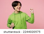 Small photo of Young happy fun man of Asian ethnicity wear green hoody doing winner gesture celebrate clenching fists say yes isolated on plain pastel light pink background studio portrait. People lifestyle concept