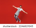 Small photo of Full body side view happy young housekeeper chef cook baker man wear grey apron look camera with outstretched hands stand on toes lean back isolated on plain red background studio Cooking food concept