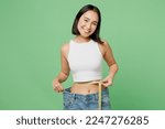 Young woman wear white clothes show loose pants after weightloss hold measure tape on waist isolated on plain pastel light green background. Proper nutrition healthy fast food unhealthy choice concept