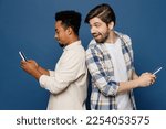 Small photo of Side view young two friends happy men wear white casual shirts together hold in hand use mobile cell phone surfing internet peep isolated plain dark royal navy blue background People lifestyle concept