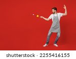 Small photo of Full body young happy male housewife housekeeper chef cook baker man wearing grey apron holding vegetables on skewer play pov fight fencing isolated on plain red background studio Cooking food concept