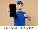 Small photo of Delivery guy employee man wearing blue cap t-shirt uniform workwear work as dealer courier hold in hand use mobile cell phone with blank screen area show thumb up isolated on plain beige background