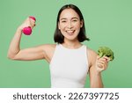 Small photo of Young happy woman wear white clothes hold in hand dumbbell broccoli vegetable show muscles isolated on plain pastel light green background. Proper nutrition healthy fast food unhealthy choice concept