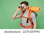 Young traveler white man carry backpack stuff mat watch in binocular isolated on plain green background. Tourist leads active healthy lifestyle walk on spare time. Hiking trek rest travel trip concept