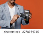 Cropped young employee business man corporate lawyer wear formal grey suit shirt work in office hold bank payment terminal process acquire credit card isolated on plain red orange background studio