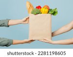 Small photo of Close up cropped female hold in hand brown paper bag with food products isolated on blue color wall background studio. Delivery service from shop or restaurant concept. Copy space advertising mock up