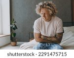 Small photo of Young sad ill man wear t-shirt pajama he sitting on bed abdomen suffering from stomach-ache griping bellyache feel bad seedy spend time in bedroom home in own room hotel wake up. Real estate concept