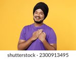 Small photo of Smiling greatful devotee Sikh Indian man ties his traditional turban dastar wear purple t-shirt put folded hands on heart isolated on plain yellow background studio portrait. People lifestyle concept